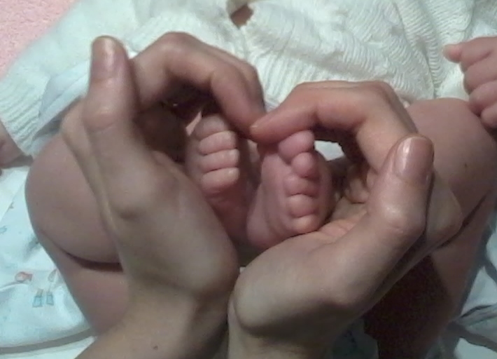 Manos de una mujer formando un corazon con los pies de un bebe dentro de ellas simbolizando el masaje metamorfico